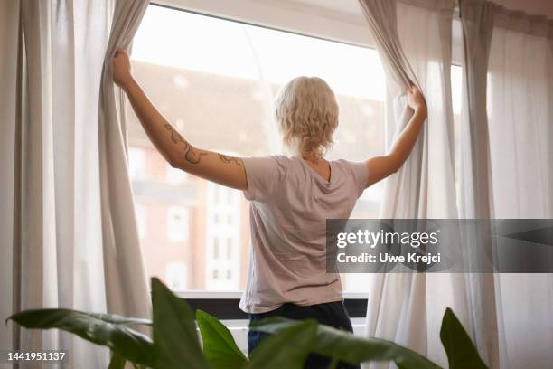 young woman opens curtains in the morning - lüften stock-fotos und bilder