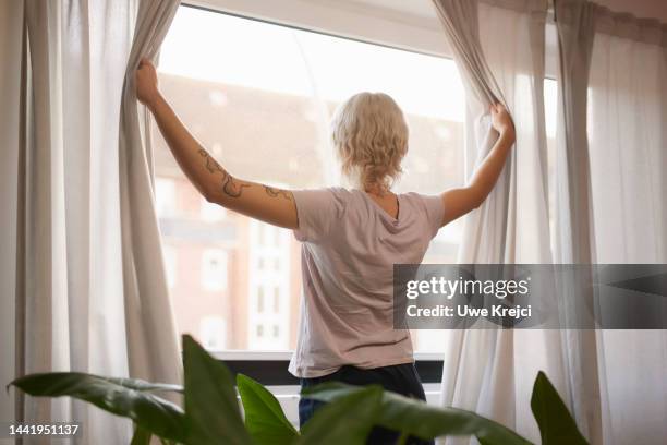 young woman opens curtains in the morning - drapery stock pictures, royalty-free photos & images