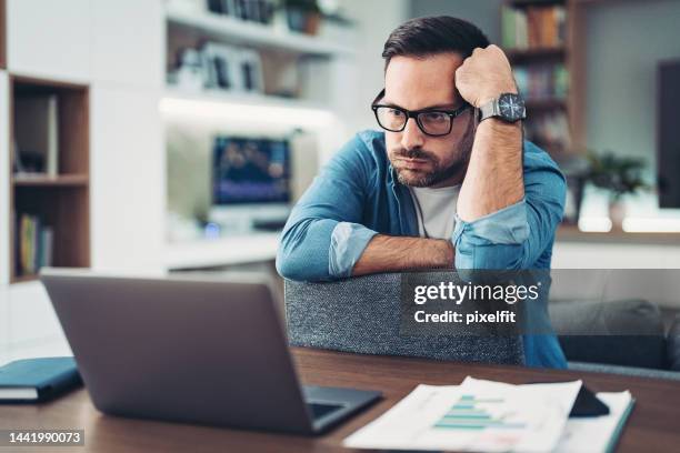 upset and worried man sitting at home in front of his laptop - crisis stock pictures, royalty-free photos & images