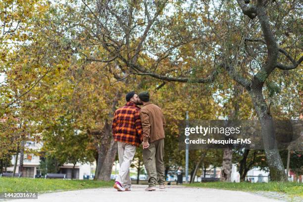 gay couple walking hand in hand in the park - mate kiss stock pictures, royalty-free photos & images