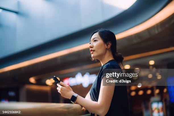 young asian woman using smartphone in shopping mall - forum shops stock-fotos und bilder