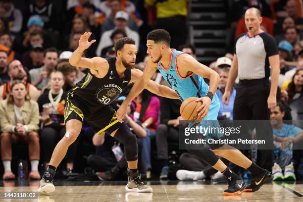 Devin Booker of the Phoenix Suns drives the ball against Stephen Curry of the Golden State Warriors during the first half of the NBA game at...