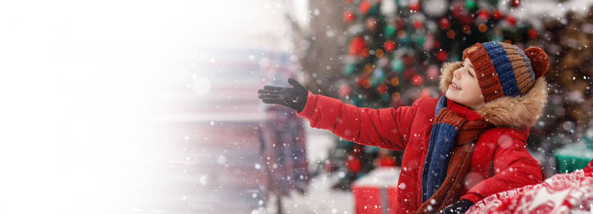 Child in red winter outerwear outdoors in snow showing hand right. New Year Christmas holiday. New year tree and presents background. Snowflakes and colorful winter clothes. Wide banner. Copy space, mock up template Child in red winter outerwear outdoors in snow showing hand right. New Year Christmas holiday. New year tree and presents background. Snowflakes and colorful winter clothes. Wide banner. Copy space, mock up template