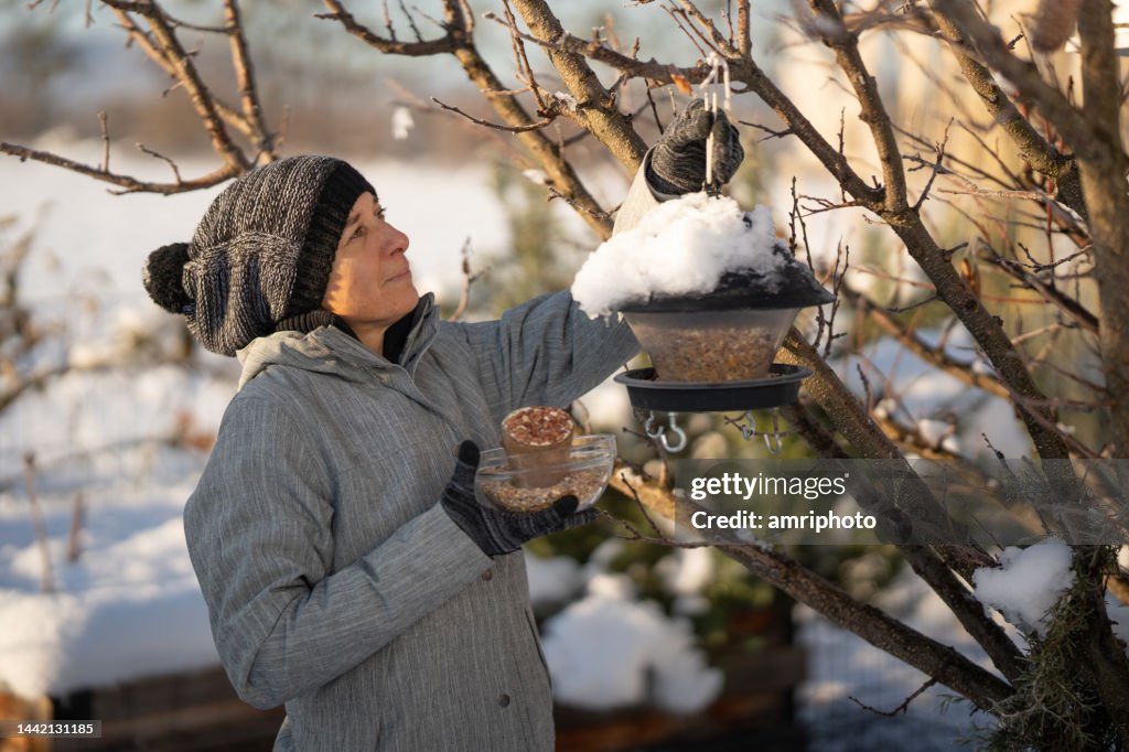 Frau am Vogelhäuschen im Garten an sonnigem Wintertag