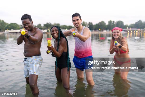 eine multirassische gruppe von freunden steht im wasser und spielt mit wasserpistolen. - african american women wet stock-fotos und bilder