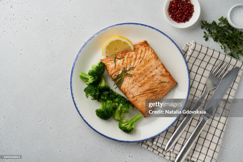 Baked sea fish and vegetables. Grilled fried salmon, broccoli, paleo, keto, lshf, fodmap or dash diet. Mediterranean food with steamed fish. Oven dish, healthy concept, gluten free, clean eating, balanced food. White ceramic plate on gray table. Top view