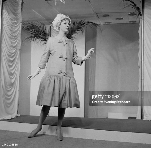 Model wearing a drop-waist cocktail coat with bow detail at a fashion show on November 23rd, 1960.