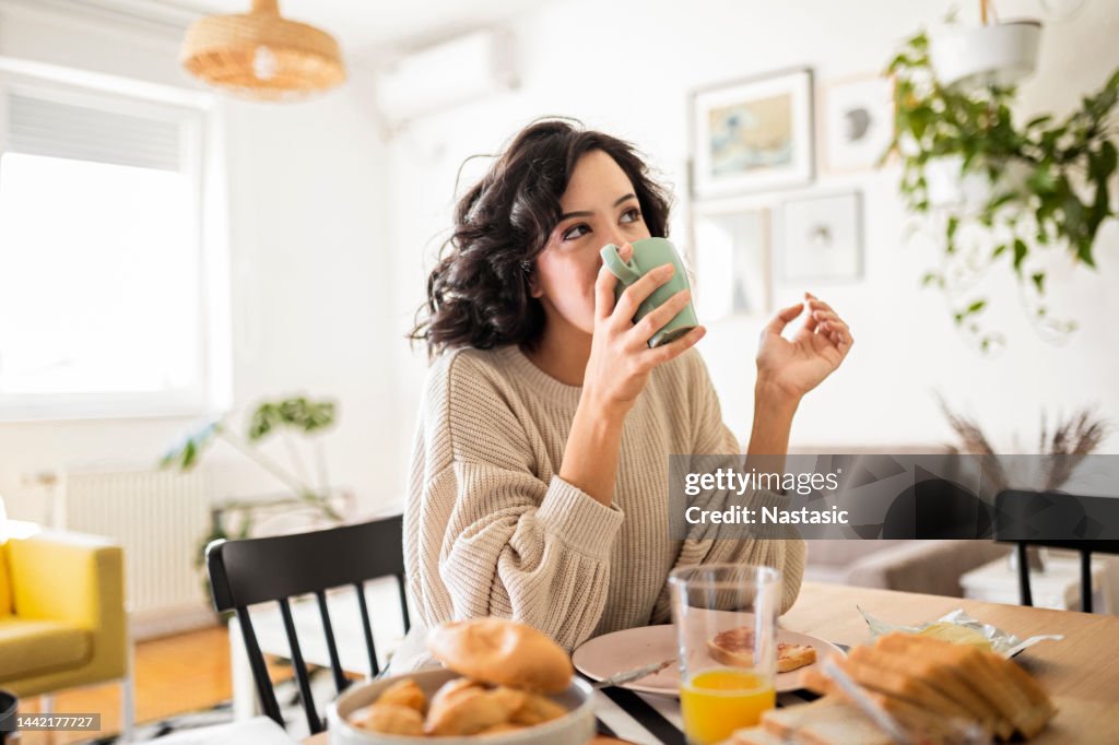 Junge Frau frühstückt zu Hause und trinkt Kaffee