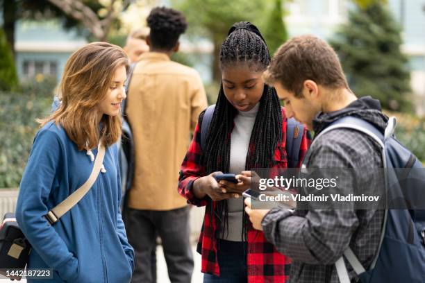 multiethnic students using their smart phones while hanging out after classes - phone transfer stock pictures, royalty-free photos & images