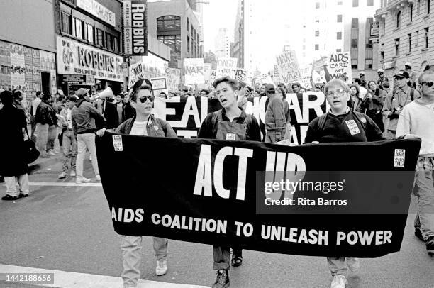 View of demonstrators, carrying an 'ACT UP' banner, during an anti-Gulf War march organized by the Coalition Against US Intervention in the Middle...