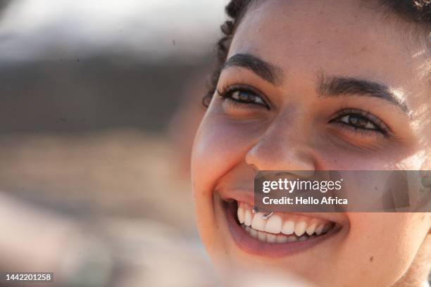 a beautiful young woman looks past camera, a twenty something wearing a smiley piercing in her mouth smiles radiantly as she looks away from camera - ethnicity fotografías e imágenes de stock