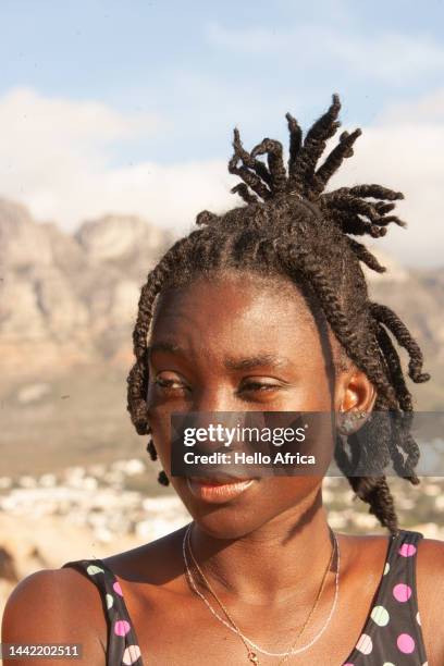 a beautiful young woman looks away from camera at an angle, a twenty something with natural braids & an afro tied up looks past camera with mountains as distant backdrop - female looking away from camera serious thinking outside natural stock pictures, royalty-free photos & images