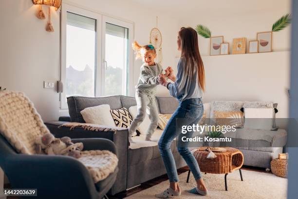happy mom and excited active daughter are dancing to music in the living room, jumping on the carpet and couch and laughing - living room kids stockfoto's en -beelden