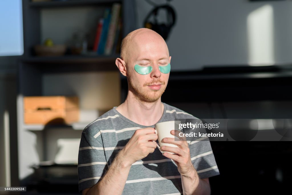 Bald man with eye patches drinking coffee