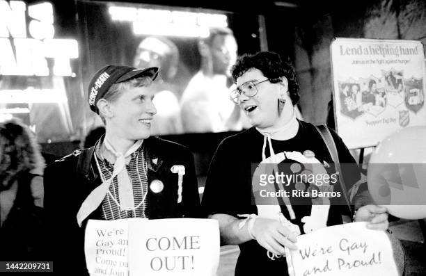 Two Queer Nation activists, each holding a sign that reads 'We're Gay and Proud,' smile at one another as they participate in a National Coming Out...