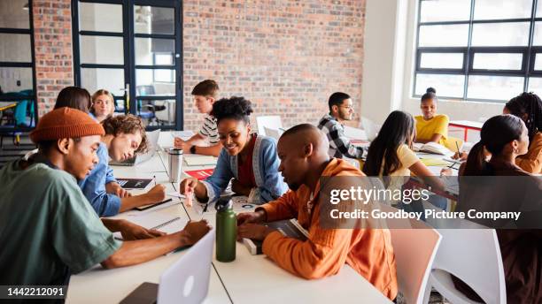 lächelnde schüler, die während einer lernsitzung an den tischen im klassenzimmer sprechen - south africa training session stock-fotos und bilder