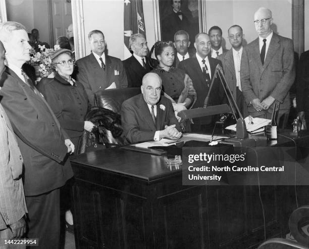 Men and women standing behind Luther H. Hodges chair in office.