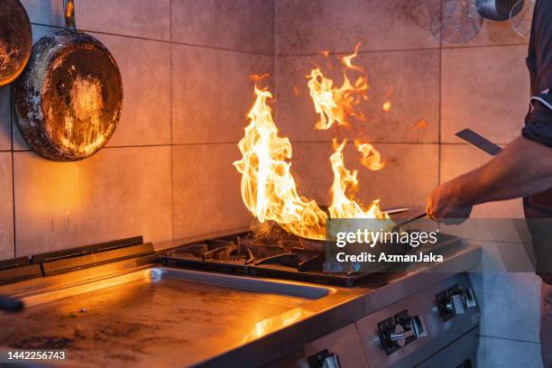primer plano de las manos de un chef caucásico flambing en el interior un ingrediente en una sartén en la cocina de un restaurante - sartenes fotografías e imágenes de stock