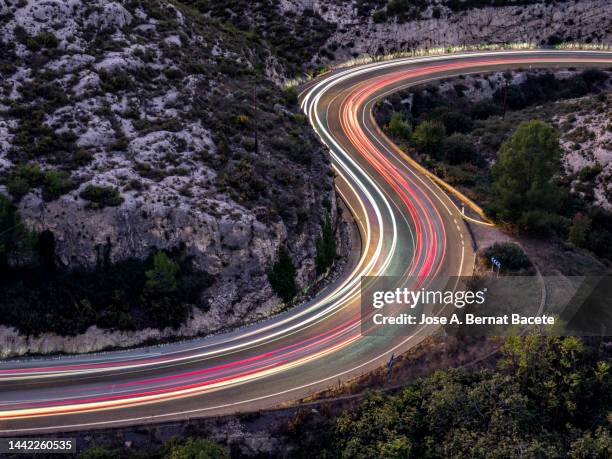 high angle view of light trails on road with curves and ravines at dusk. - vehicle light fotografías e imágenes de stock