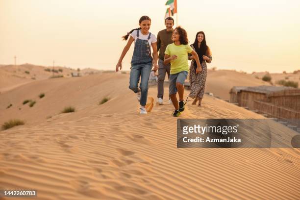 middle eastern family running across the dunes in dubai - middle east desert stock pictures, royalty-free photos & images