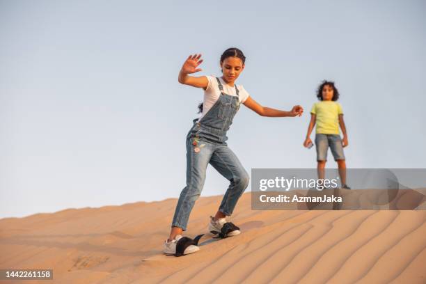 teenage girl sandboarding down the dune in dubai - sand boarding stock pictures, royalty-free photos & images