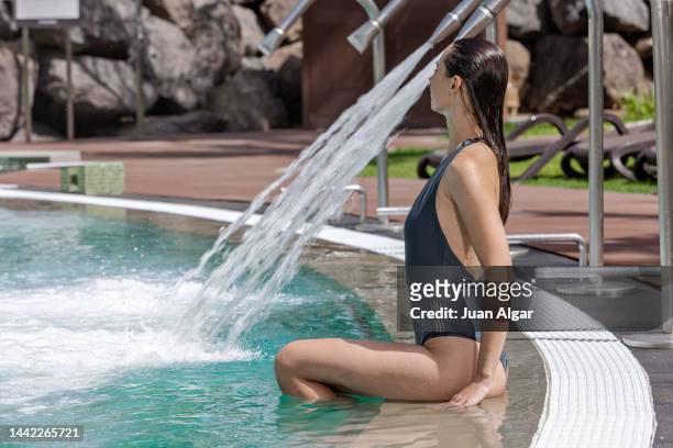 woman sitting on poolside near spa shower in pool - algar waterfall spain stock pictures, royalty-free photos & images