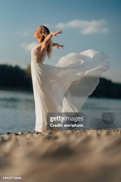 sposa elegante in abito da sposa bianco sulla spiaggia del fiume - vestito bianco foto e immagini stock