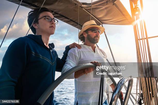 a father teaches his son to sailboat and guides him. - father son sailing stock pictures, royalty-free photos & images