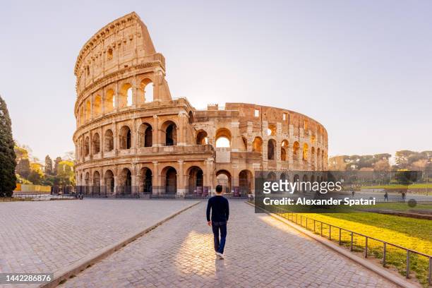 rear view of a man walking towards coliseum, rome, italy - coliseo romano fotografías e imágenes de stock