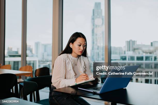 a young woman looks anxious as she takes notes as she looks at her laptop - studying stock pictures, royalty-free photos & images