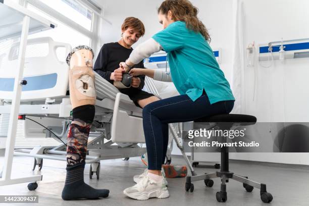 female physiotherapist helping young man with prosthetic leg at hospital - diabetes feet stock pictures, royalty-free photos & images