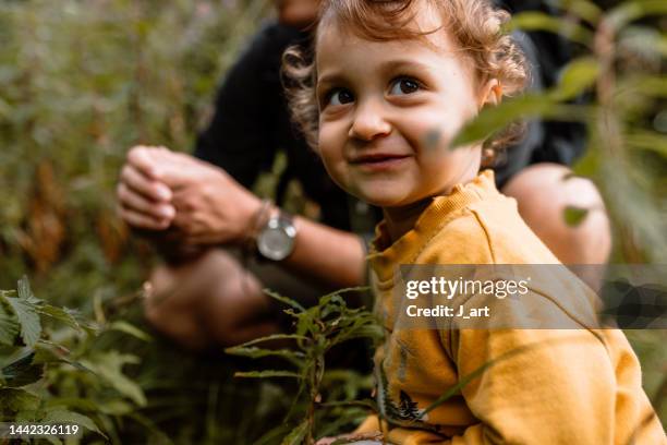 portrait of a smiling toddler girl crouching in the grass and exploring the nature. - explorer stock-fotos und bilder