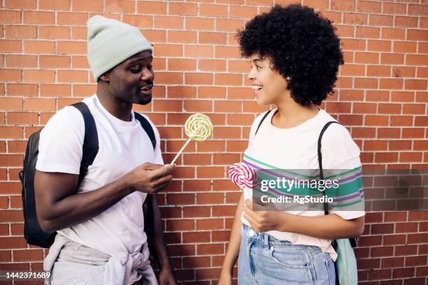 happy afro couple eating lollipops and having fun - lollipop man stockfoto's en -beelden