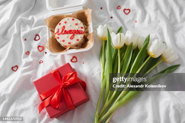 tasty bento cake, red gift present and bouquet of white tulips on white bed. valentine's day concept. directly above - heart box ribbon stockfoto's en -beelden