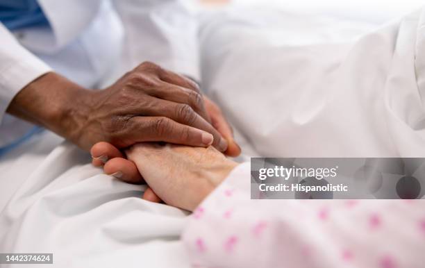 primo piano su un medico che tiene la mano di una donna malata nel letto dell'ospedale - ospizio foto e immagini stock
