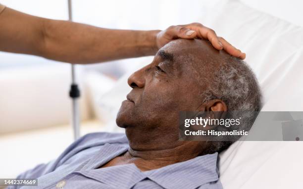 close-up on a sick senior adult being visited at the hospital by his son - hospice stock pictures, royalty-free photos & images