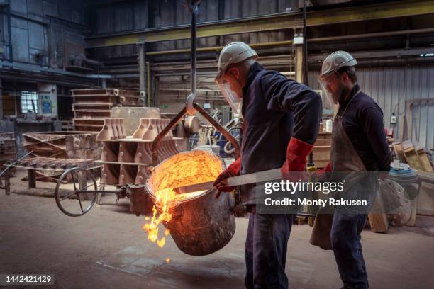 worker skimming top of ladle of molten brass in brass foundry - metalwork stock-fotos und bilder