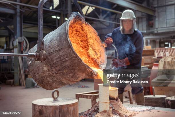 worker pouring molten brass into large mold in brass foundry - ferronnerie photos et images de collection