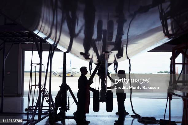 silhouettes of aircraft engineers inspecting landing gear on large jet - landing gear stock-fotos und bilder