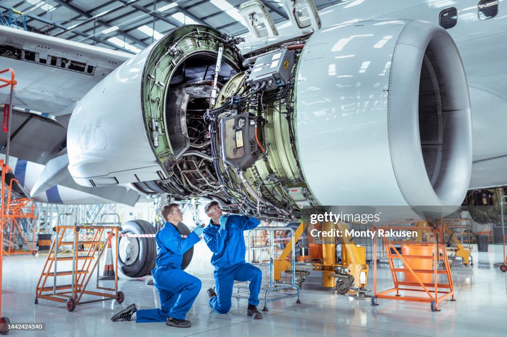 Apprentice aircraft maintenance engineers work underneath large jet engine