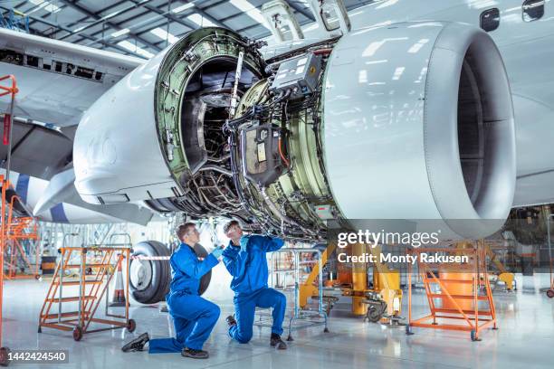 apprentice aircraft maintenance engineers work underneath large jet engine - vliegtuigmonteur stockfoto's en -beelden
