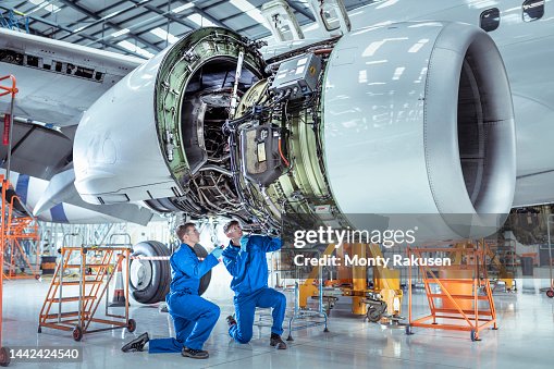 Apprentice aircraft maintenance engineers work underneath large jet engine Apprentice aircraft maintenance engineers work underneath large jet engine
