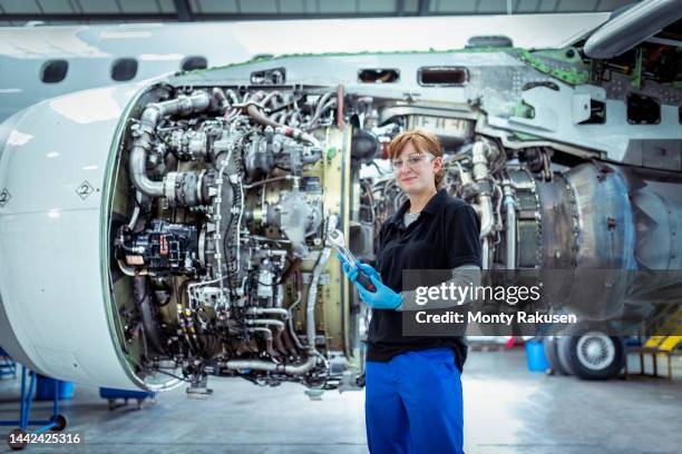 portrait of female apprentice aircraft maintenance engineer with jet engine - vliegtuigmonteur stockfoto's en -beelden