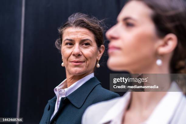 mujer de negocios madura y rica con una hija de mediana edad que tiene una conversación tranquila en lugares al aire libre de una ciudad premium sobre negocios familiares - continuidad fotografías e imágenes de stock