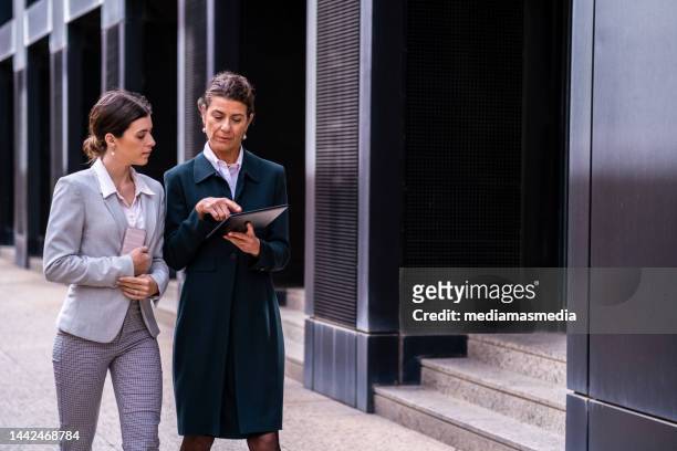 mature and wealthy senior business woman with a middle-aged daughter having a calm conversation in a premium city outdoor locations about family business - successor stockfoto's en -beelden