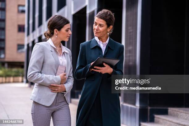 mature and wealthy senior business woman with a middle-aged daughter having a calm conversation in a premium city outdoor locations about family business - successor stockfoto's en -beelden