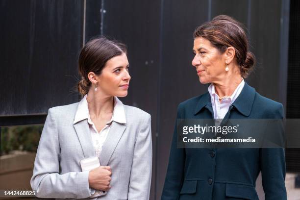 mature and wealthy senior business woman with a middle-aged daughter having a calm conversation in a premium city outdoor locations about family business - bank manager imagens e fotografias de stock