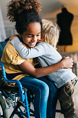 Black little girl with disability in wheelchair hugging with her younger brother.