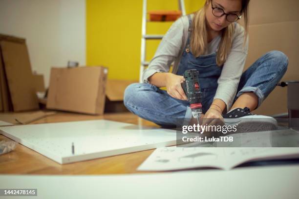 una mujer que usa tirantes usa una herramienta eléctrica inalámbrica - women in suspenders fotografías e imágenes de stock