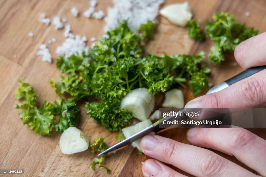 Chopping garlic and parsley on a wooden cutting board